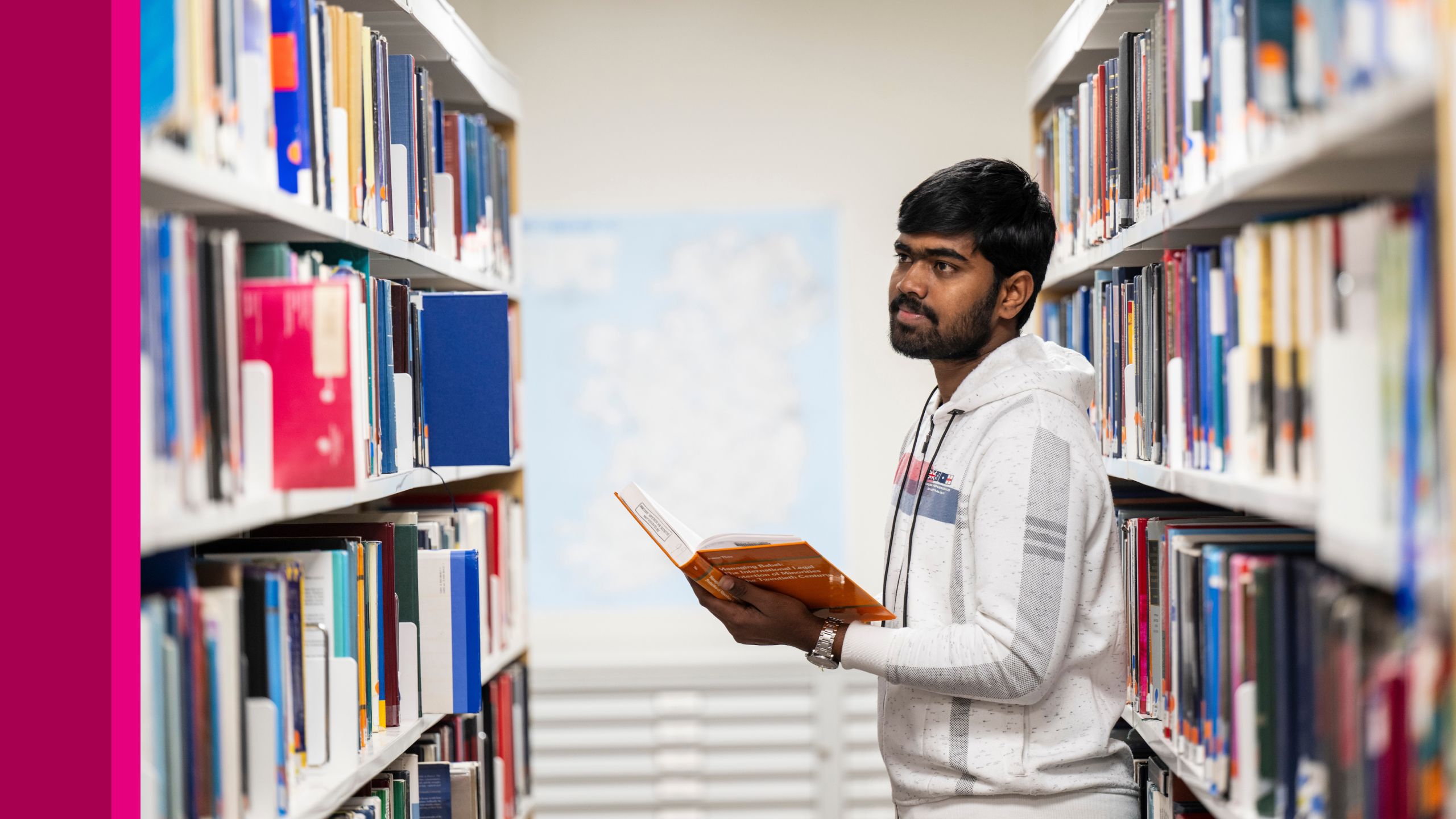 A student with a book in his hand looking at other books on a shelf