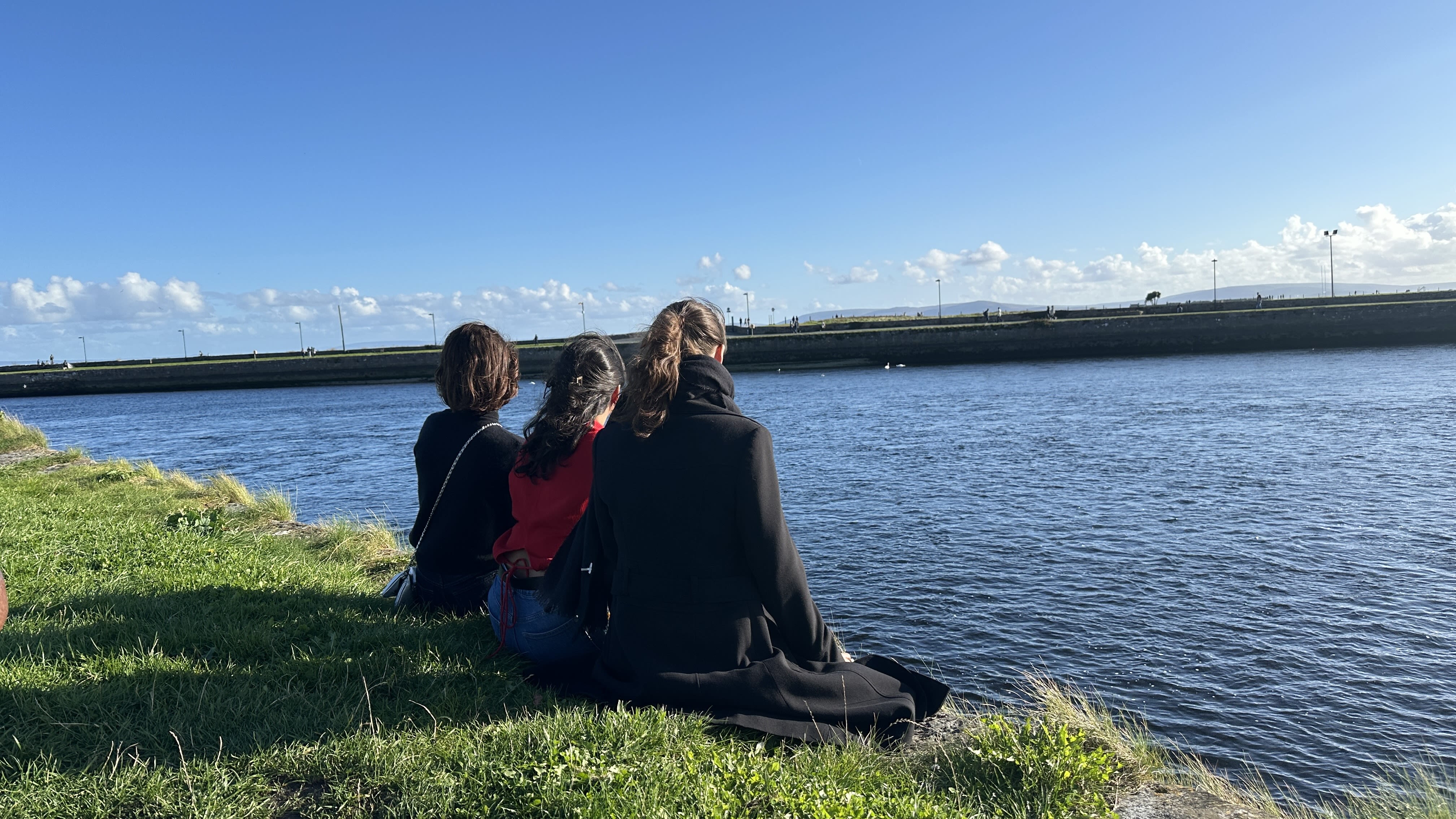 Three friends sitting on a wall over looking Galway's Corrib River